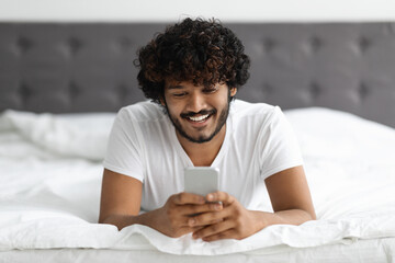 Portrait of handsome hindu guy laying on bed with phone