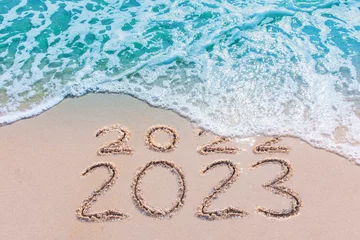 Tuinposter Message Year 2022 replaced by 2023 written on beach sand background. Good bye 2022 hello to 2023 happy New Year coming concept.  © MAITREE
