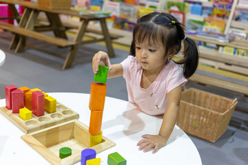 Focus on hands of little child girl playing with colorful wooden blocks in the room