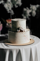 A wedding cake. Milk-colored cake decorated with cotton beads and gold leaf on a dark background in wedding day