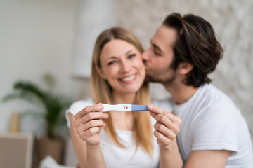 Happy young couple showing positive pregnancy test and kissing at home, selective focus © Prostock-studio