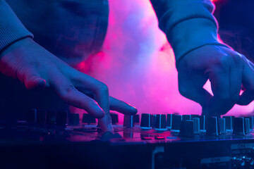 Close-up image in neon lights. Male hands turning sounds on professional dj mixer. Creative soundmaker