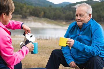 Senior couple camping outdoor having fun drinking coffee in mountain lake - Elderly travel vacation