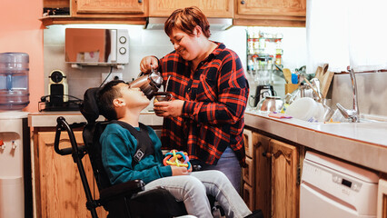 Latin mother taking care of son with disability on wheelchair inside home kitchen - Focus on mom face - obrazy, fototapety, plakaty