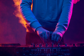 Close-up image in neon lights. Male hands turning sounds on professional dj mixer. Smoked effect