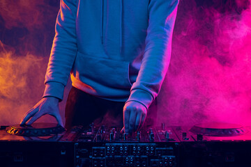 Close-up image in neon lights with smoke effect. Male hands turning sounds on professional dj mixer