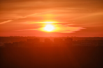 Evening sun in continuous cloudiness on a hot foggy sky above the silhouettes of city buildings. Sunset in a haze of thick clouds over the houses in the urban landscape