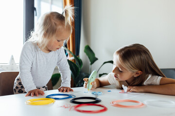 cute little caucasian girl eight years old drawing different things by 3d pen with a green handle. Her baby sister looking to table. STEM educational toy for kids at home and school. Play and study