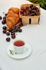 Black tea with fresh croissants and cherries on the table against white background. Flat lay, spring breakfast conceptual composition