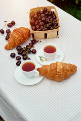 Black tea with fresh croissants and cherries on the table against white background. Flat lay, spring breakfast conceptual composition