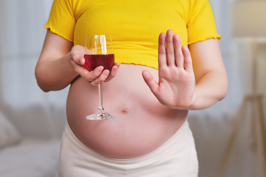 A pregnant woman holds a glass of red wine in her hand and shows a stop sign