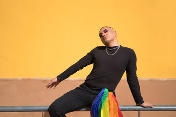 Non-binary person, young South American, heavily make up, sitting on a railing with a gay pride...
