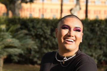 Portrait of non-binary person, young and South American, heavily make up, smiling happily, getting...