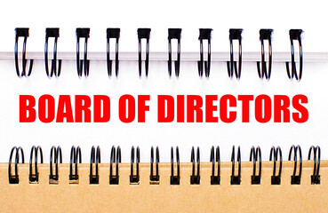 Text BOARD OF DIRECTORS on white paper between white and brown spiral notepads.