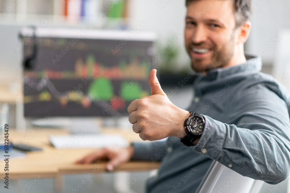 Poster Positive mature businessman working on computer with graphs and charts on screen, showing thumb up, selective focus