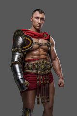Studio shot of roman gladiator with muscular build and naked torso dressed in armor and cloak.
