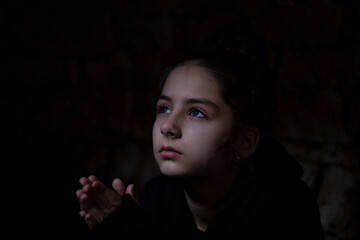 War in Ukraine. A child in a bomb shelter prays to God for peace in her country. Portrait of the...