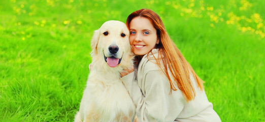 Portrait of happy smiling woman with her Golden Retriever dog on green grass in summer park