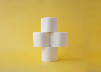 On a yellow background, four rolls of toilet paper stand on top of each other