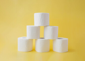On a yellow background, six rolls of toilet paper stand in the form of a pyramid