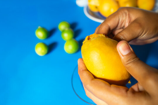 Closeup of the hand of a Latin woman peeling a mango with a blue background with jocotes and typical summer fruits in Nicaragua, Central America and Latin AmericaCloseup of the hand of a Latin woman