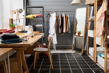 Interior of spacious workshop of modern fashion designer with large mirror, shelves, folded textile and sewing machine on table