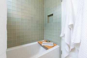 Sleek bathroom tub with blue green tile, spa tray and white towels.