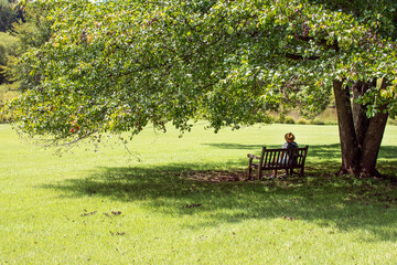woman tourist in  hat is resting on bench in the shade of  tree in the park