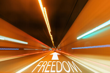 Text freedom and written on the straight road with an arrow in a tunnel with a blurred light. Concept of change of lifestyle and goal. 