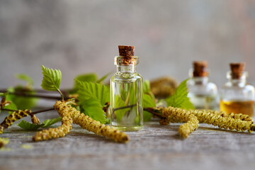 A bottle of essential oil with birch branches on a table