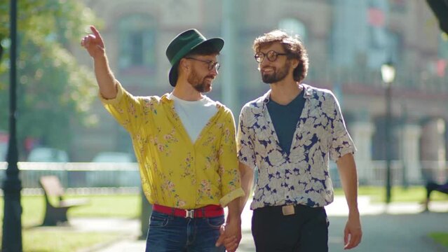Stylish two gay men walking look to each other in eyes holding hands homosexual couple dating LGBT relationship love smiling outdoors boyfriend attractive slow motion