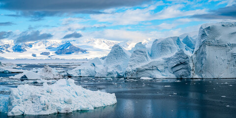 Tabular Iceberg in front of Antarctic Peninsula pictured inside Larsen A inlet with a very scenic cloudy sky and mountains at the backgound - obrazy, fototapety, plakaty