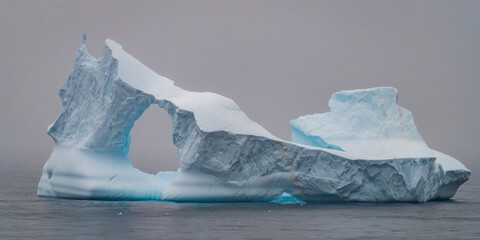 Iceberg in Antarctica with fog around and a good visible see through hole and and an artistic shape..