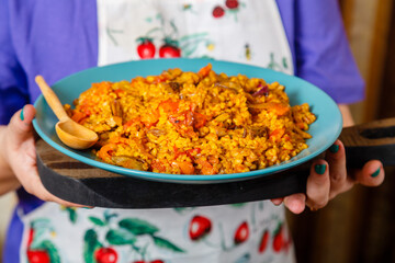 A dish with bulgur and vegetables and a wooden spoon in female hands.