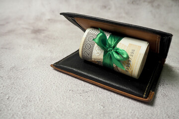 200 Polish zloty are in a black and brown leather wallet with a green ribbon on a gray background. ...