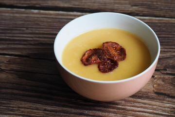 a round plate of vegetable soup mashed potatoes, carrots, onions, parsley root, a seller decorated with three chips of dried tomatoes stands on a brown wooden table. restaurant. gluten-free.