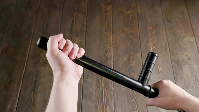 caucasian hands holding black rubber police tonfa baton over wooden surface. Someone menacingly pats himself on the hand with a nightstick.