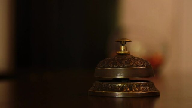 call on a old hotel bell on a wood stand. the visitor's hand calls the concierge at the hotel reception in the reception bell. at first once, then repeatedly presses the button