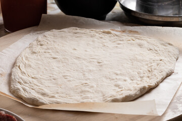 Rolled out pizza dough on baking paper. Process of making pizza
