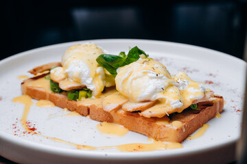 Toast with egg poached, healthy breakfast of waffles, poached egg with bacon and arugula. Brioche sandwich