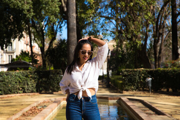 Young, beautiful, brunette woman on the edge of a fountain in the park in seville. The south american woman is on tourism in europe and is enjoying her holidays.