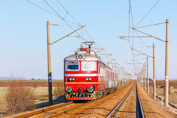 A red electric locomotive pulls the carriages of a high-speed intercity passenger train along the...