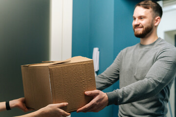 Side view of friendly bearded courier male delivering cardboard box parcel to female customer on...