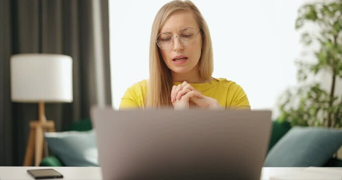 Confident mature woman in eyeglasses and casual wear sitting at home office and using modern laptop for video conference. Concept of people, technology and online communication.