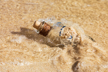 Strandgut, alte leere Flasche an einem Strand im Sand umspült vom Wasser an der Küste.