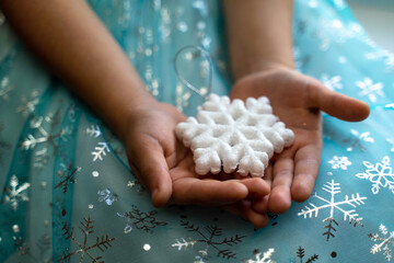 Winter and Christmas concept. Children's hands close-up holding a magic snowflake on the background of a blue dress with snowflakes.