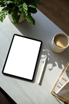Blank tablet mockup on table. Aesthetic home office desk with tablet, pen, cup of coffee, office stationery, green plant.