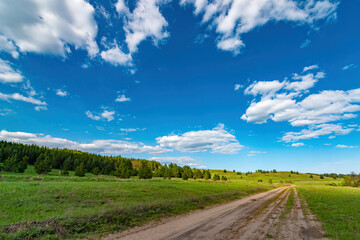 Fototapeta na wymiar Dirt road rural countryside leading to the top of the hill, blue dramatic storm clouds at summertime