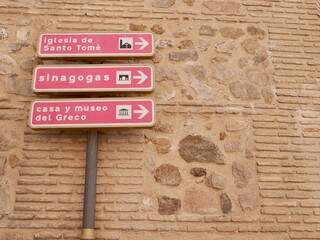 Close up of sign indicating direction to Synagogues, church Santo Tomé and El Greco museum. Toledo, Castile La Mancha, Spain. - obrazy, fototapety, plakaty