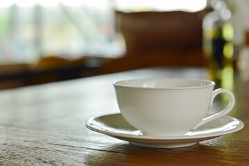 A one white cup of hot coffee on wooden table in blur coffee shop background.